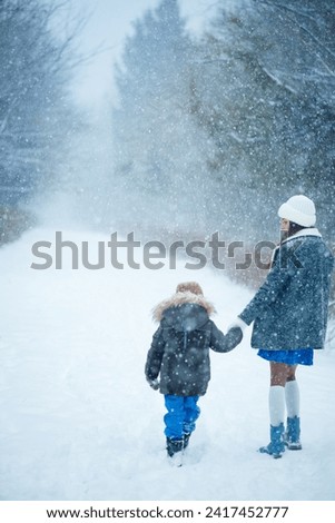 Mother and son are walking in the forest in winter. It is snowing heavily. Children's happiness. Warm clothes in January