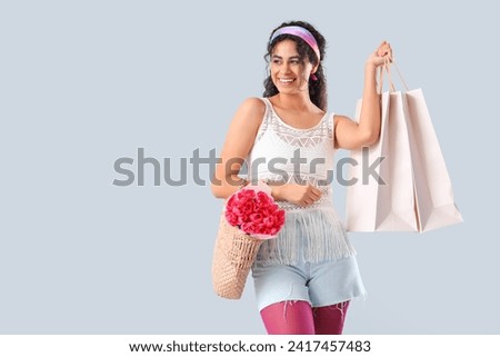 Fashionable African-American woman with bouquet of flowers and shopping bags on white background. International Women's Day celebration