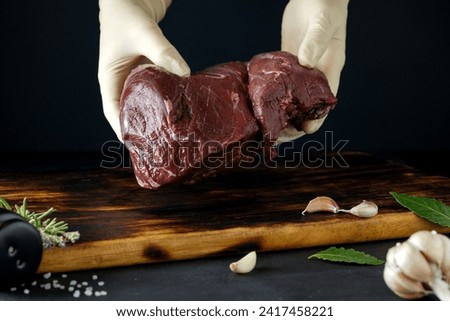 A large piece of venison in the hands of the cook. Black background Royalty-Free Stock Photo #2417458221
