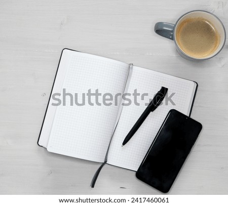 open white notebook, a black mobile phone and a cup of coffee on light wooden background