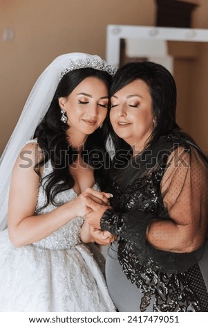 A beautiful and happy mother and her daughter, the bride, are standing next to each other. The best day for parents. Tender moments at the wedding. Royalty-Free Stock Photo #2417479051