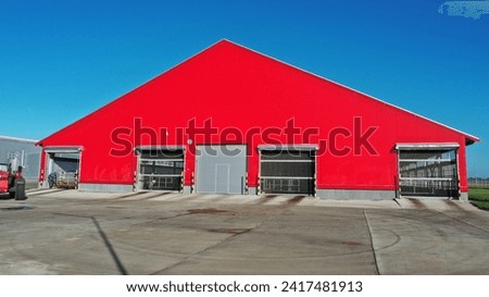The barn is red in color. A building for keeping cows in winter in the cold season. Where cattle live on a dairy farm in winter. Red huge shed for animals. Red facade of a building made of metal struc