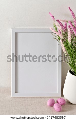 Easter holiday poster template for social media blog or business branding, blank white picture frame mockup, spring flowers in vase, small pink candy eggs on beige linen table background.