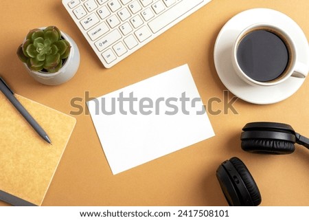 Desktop with blank card, coffee cup, notepad, keyboard, succulent plant and headphones on brown table. Top view, flat lay, mockup