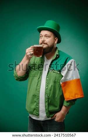 Happy bearded man with glass of beer and Irish flag on dark green background. St. Patrick's Day.