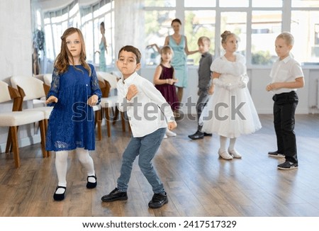 Excited preteen children, boy and girl in party attire artistically performing twist in sunny dance room as female teacher supervising with smile in background