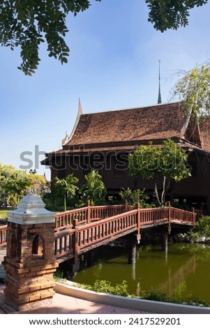 A wooden bridge extends over a serene pond, offering a picturesque view in front of a stately building. Royalty-Free Stock Photo #2417529201