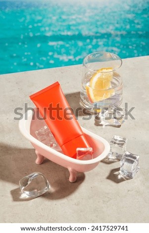 Red tube of sunscreen placed inside a bathtub. A lot of ices scattered on the surface. A cup of detox water featured. The concept of summer holidays, beauty and sunscreen for skin