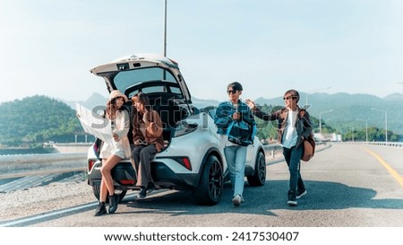 Group of Happy Asian man and woman enjoy and fun outdoor lifestyle road trip travel nature countryside on summer holiday vacation. Generation z people friends sitting on car trunk and looking on a map Royalty-Free Stock Photo #2417530407