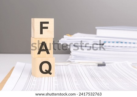 FAQ text on wood blocks on a document with tables on a stack of documents in the gray background