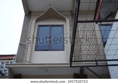 The upper side of the glass window of the mosque building is ornate with brown walls