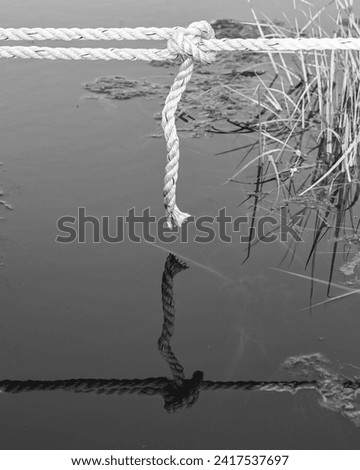 black and white photo of a rope with a knot tied to a boat and its reflection in the water