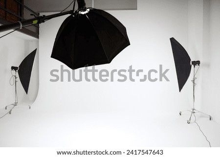 photo studio inside, white background, several racks with light sources, cyclorama, softboxes, pulsed light, flashes