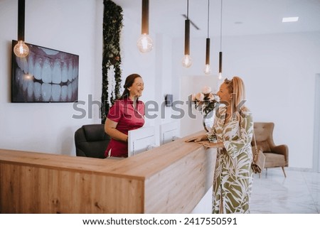 A beautiful blonde woman conversing with the dental clinic receptionist, scheduling an appointment for dental treatment with a bright smile Royalty-Free Stock Photo #2417550591