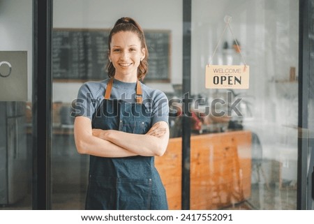 Portrait of happy waitress standing at restaurant entrance with open sign, Portrait of young business woman attend new customers in her coffee shop. Royalty-Free Stock Photo #2417552091
