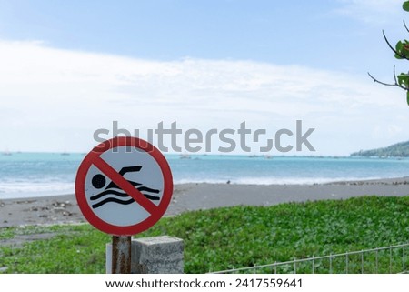 Sign, no Swimming on the Beach with a blurry beach as a background