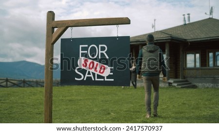 For sale sign on beautiful green lawn. African American real estate agent comes and puts sold sticker on sign. Modern cottage with traditional architecture in mountains. Residential property on sale.