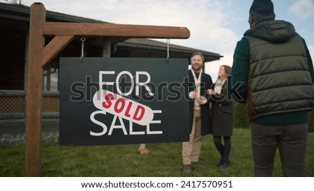 For sale sign on beautiful green lawn. African American real estate agent comes and puts sold sticker on sign. Modern cottage with traditional architecture in mountains. Residential property on sale.