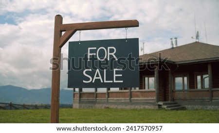 For sale sign on beautiful green lawn. Modern house for sale in mountains with amazing landscapes. Stylish property with traditional architecture. Concept of residential property on sale.