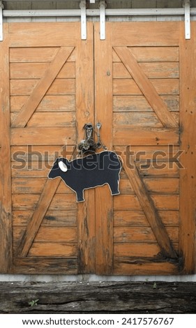 ฺBrown wooden door on sheep farm.Sign with picture of sheep on wooden wall. Farm animal