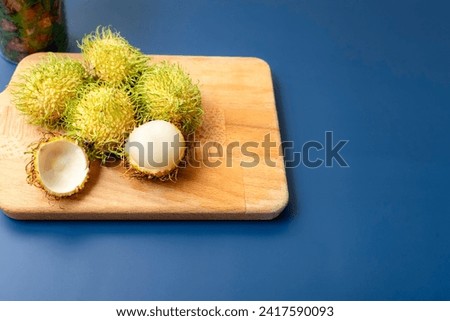 A group of yellow tropical rambutans (scientific name: Nephelium lappaceum) on brown cutting board; with dark blue background. A close-up and selective focus photo of the rambutan flesh.