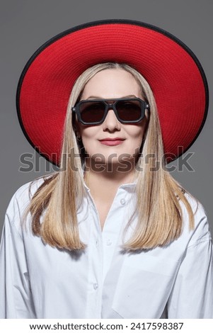 Portrait of a beautiful mature woman in a white blouse, hat, and fashionable glasses. Light gray studio background. Business style and fashion.