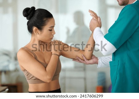 Patient complaining about muscle tension in her arm when visiting physiotherapist Royalty-Free Stock Photo #2417606299
