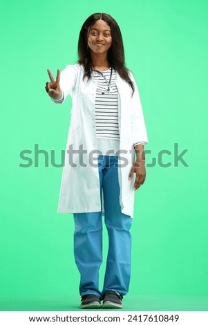 A female doctor, on a green background, in full height, shows a victory sign
