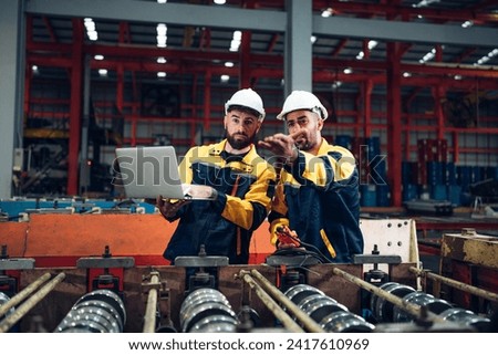 Industrial man engineer wear uniform and helmet using laptop are checking system machine at factory. Workers industrial factory. Machine maintenance technician operation concept.