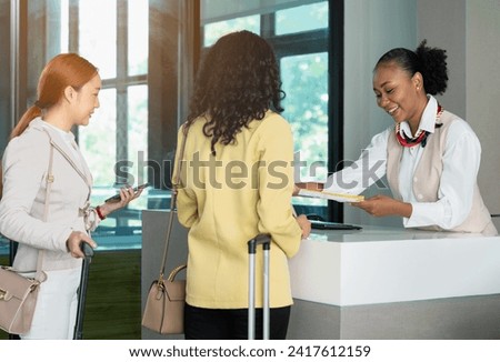 African woman airline ground staff giving boarding pass or ticket to businesswoman passenger at airport check in counter. Business trip concept Royalty-Free Stock Photo #2417612159