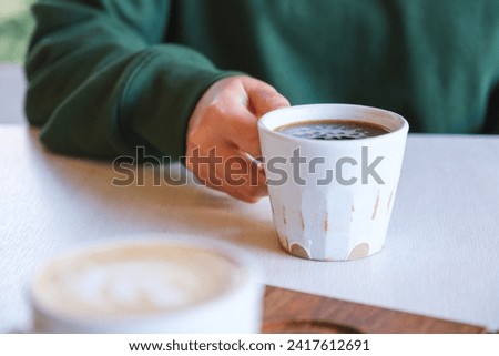 Closeup image of a woman holding and drinking coffee with friend in cafe