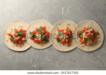 Delicious tacos with vegetables and parsley on grey marble table, top view