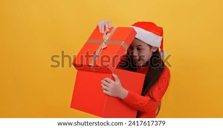 Cute little girl wearing a Christmas costume holding a big gift box. Isolated on yellow background in studio.