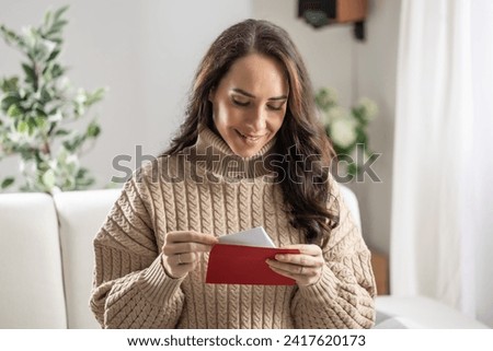 A good-looking brunette reads a love letter with a red envelope that she received from her boyfriend. Royalty-Free Stock Photo #2417620173