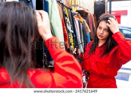 Woman looking in the mirror while shopping in a second hand store Royalty-Free Stock Photo #2417621649