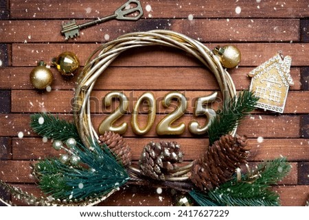New Year House key with keychain cottage on festive brown wooden background with number 2025 in wreath, lights of garlands. Purchase, construction, relocation, mortgage, insurance