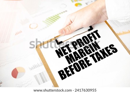 Text NET PROFIT MARGIN BEFORE TAXES on white paper plate in businessman hands with financial diagram. Business concept