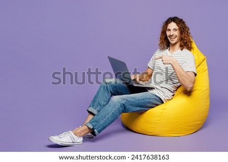 Full body young IT man wear grey striped t-shirt casual clothes sit in bag chair hold use work point on laptop pc computer isolated on plain pastel light purple background studio. Lifestyle concept