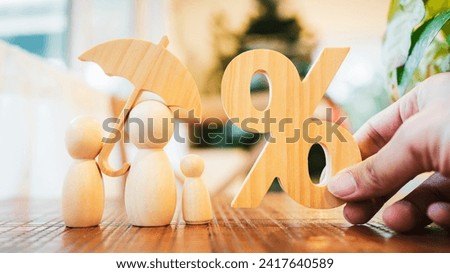 A picture of a wooden model and a family of parents and children holding an umbrella biting a percentage symbol. The picture is a picture with a concept about insurance planning.