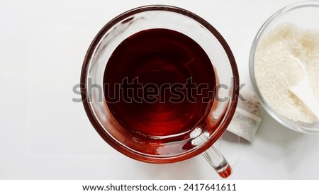 Close up picture from the top, angles of a clear cup of tea and a small clear bowl of granulated sugar isolated on a white background. Concept for drinks with sugar contain.