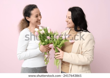 Happy mature women with bouquets of beautiful tulips on pink background. International Women's Day