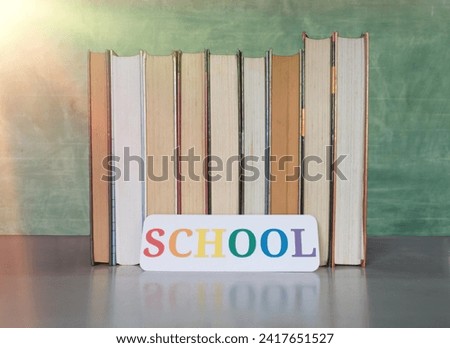 stack of textbooks and school sign on desk over blurred blackboard in classroom