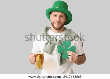 Young man in leprechaun hat with glass of beer and clover on grey background. St. Patrick's Day celebration