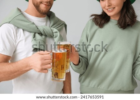 Beautiful young couple with glasses of beer on grey background. St. Patrick's Day celebration