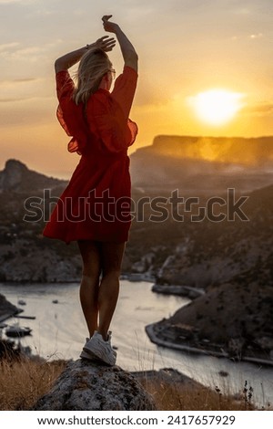 Happy woman standing with her back on the sunset in nature in summer with open hands posing with mountains on sunset, silhouette. Woman in the mountains red dress, eco friendly, summer landscape