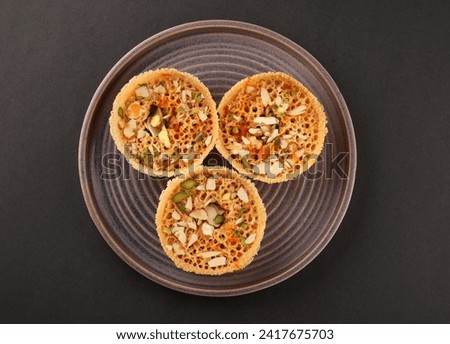 Indian Rajasthani crunchy sweet dish called Ghevar or Ghewar is an made using refined flour, sugar, and ghee. Garnished with silver foil and dry fruits  Royalty-Free Stock Photo #2417675703