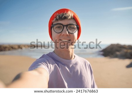 Un hombre feliz se toma una selfie en la playa - Un turista masculino disfruta de sus vacaciones de invierno - Un tipo suena como si la cámara brillara - Lo mira a los ojos.