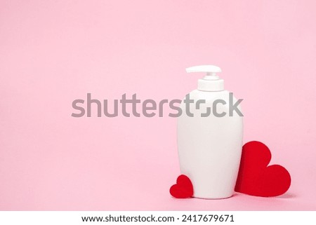 White cosmetic bottle with shampoo, soap or body lotion and red hearts on pink background, copy space