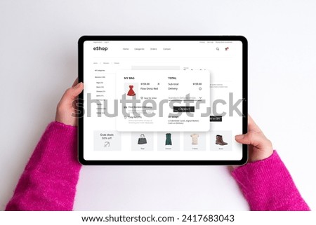 E-commerce cart page on a tablet with price, delivery options, and checkout button. Woman buys a red dress, creating a seamless and stylish online shopping experience Royalty-Free Stock Photo #2417683043