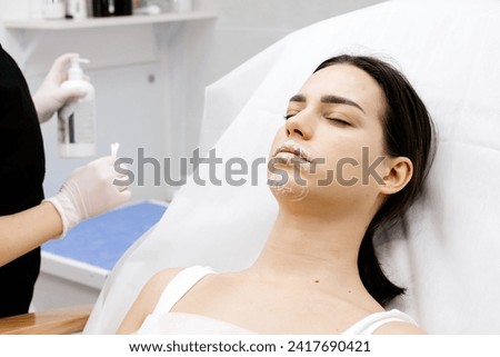 Cosmetology clinic, the doctor applies anesthesia to the patient's lips, anesthetic before injecting hyaluronic acid. Anesthetic ointment is applied before the injection procedure. Royalty-Free Stock Photo #2417690421